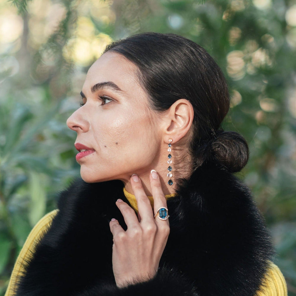 
                  
                    Model demonstrating the wear of the Luxury gemstone jewelry piece, the Long Teal Topaz and White Topaz Drop Earrings in 18ct Yellow Gold and the Gstaad Statement Ring – Gstaad Collection, Augustine jewelry, Luxury jewelry London.
                  
                