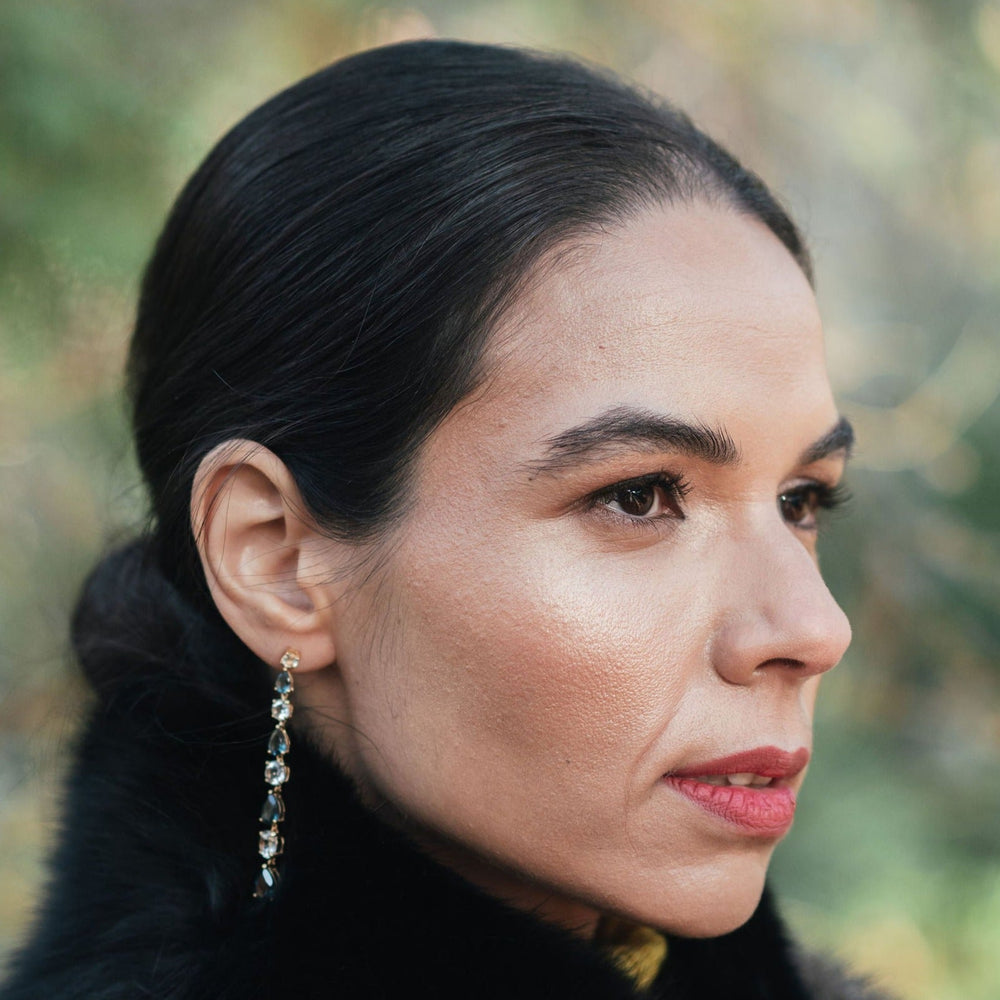 Model wearing long teal topaz and white topaz drop earrings in yellow gold