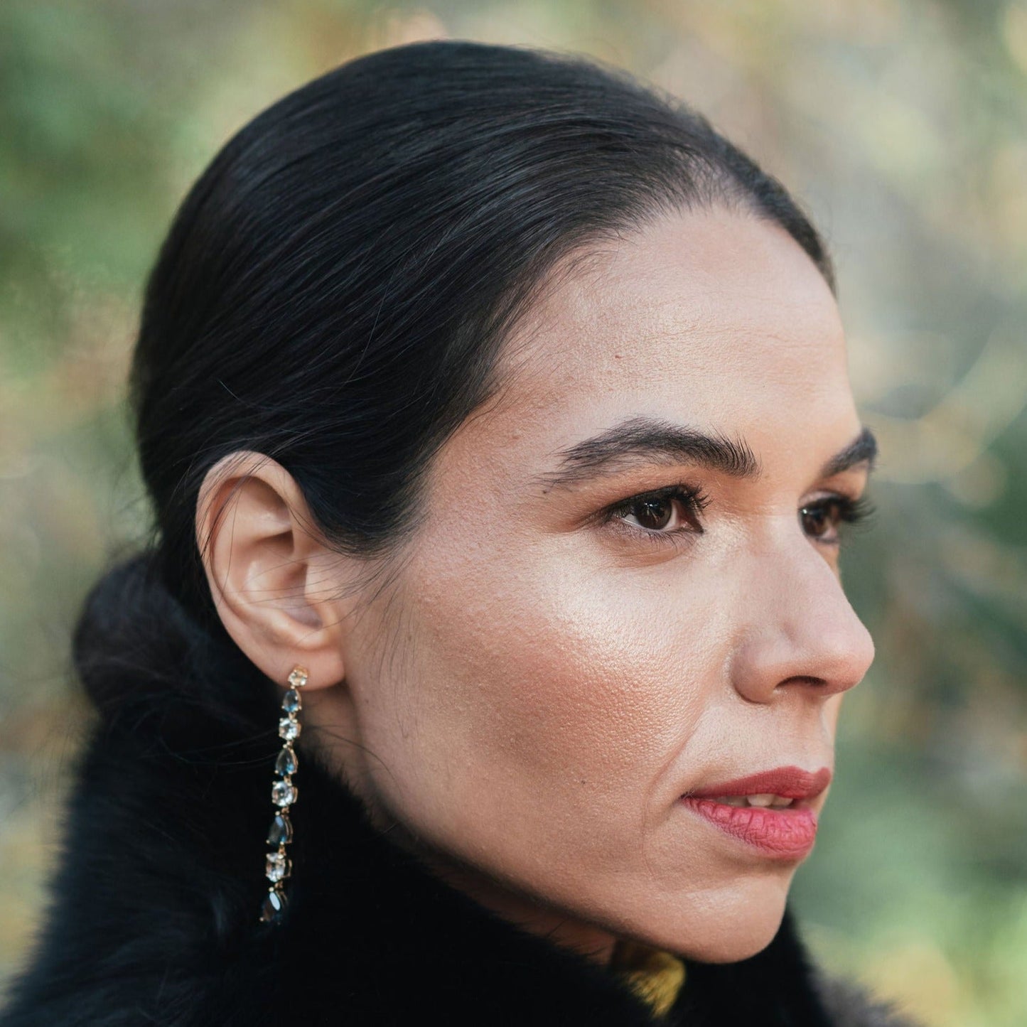 Model wearing long teal topaz and white topaz drop earrings in yellow gold