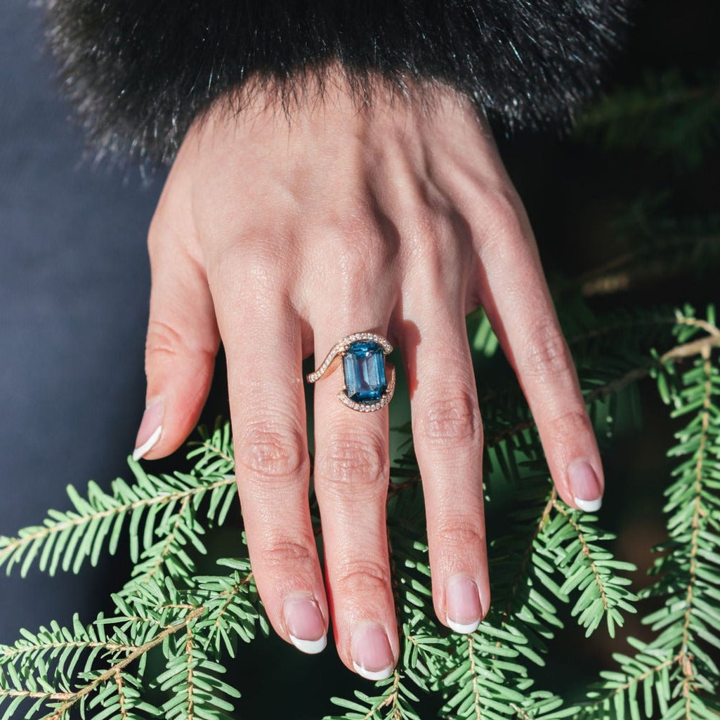 Model wearing diamond ring with teal topaz in wedeln design in 18ct yellow gold