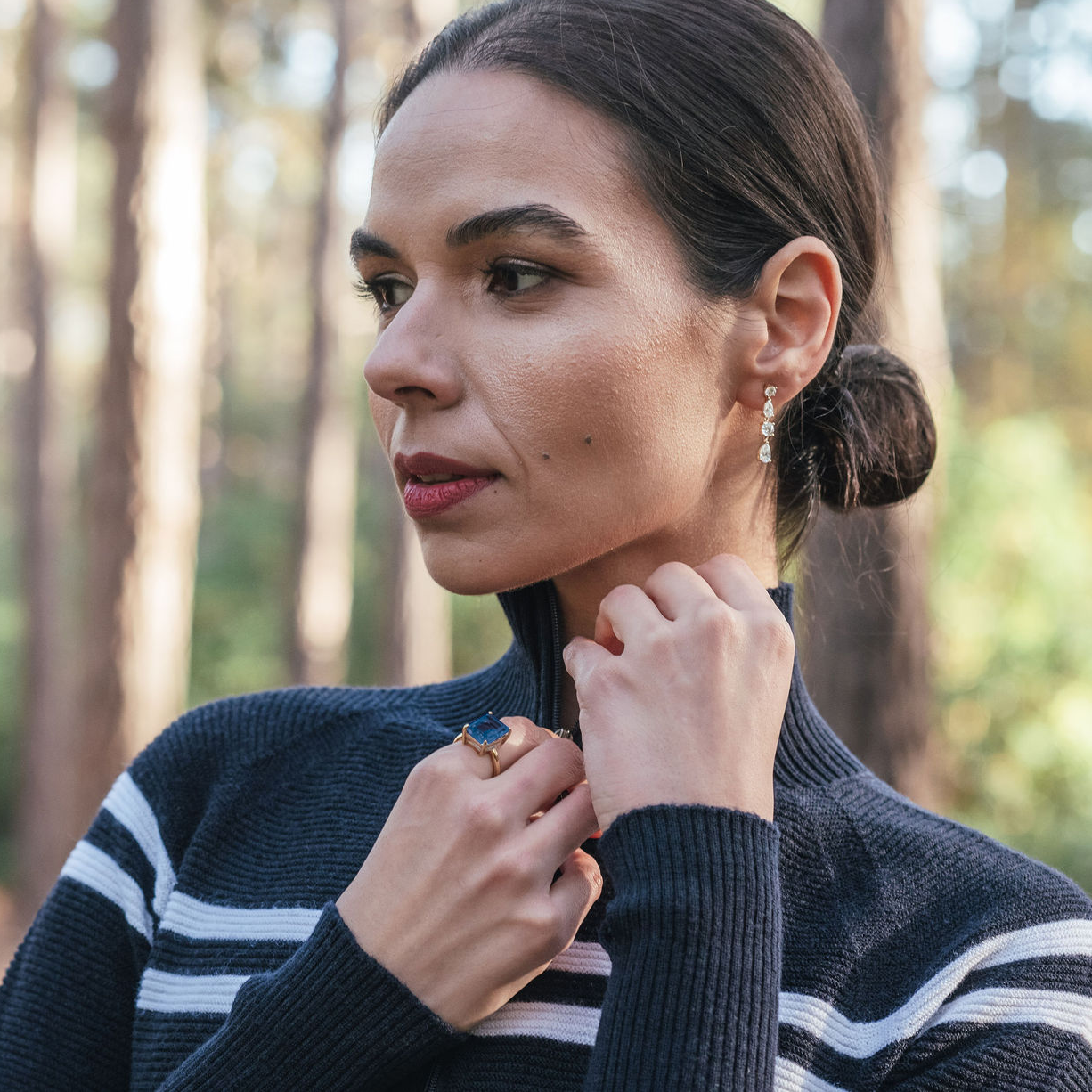 Model demonstrating the wear of the luxury gemstone jewelry piece, the Teal Topaz Cocktail Ring with Sterling Silver band and Gstaad Short Diamond Earrings   – Gstaad Collection, Augustine jewelry, Luxury jewelry London.